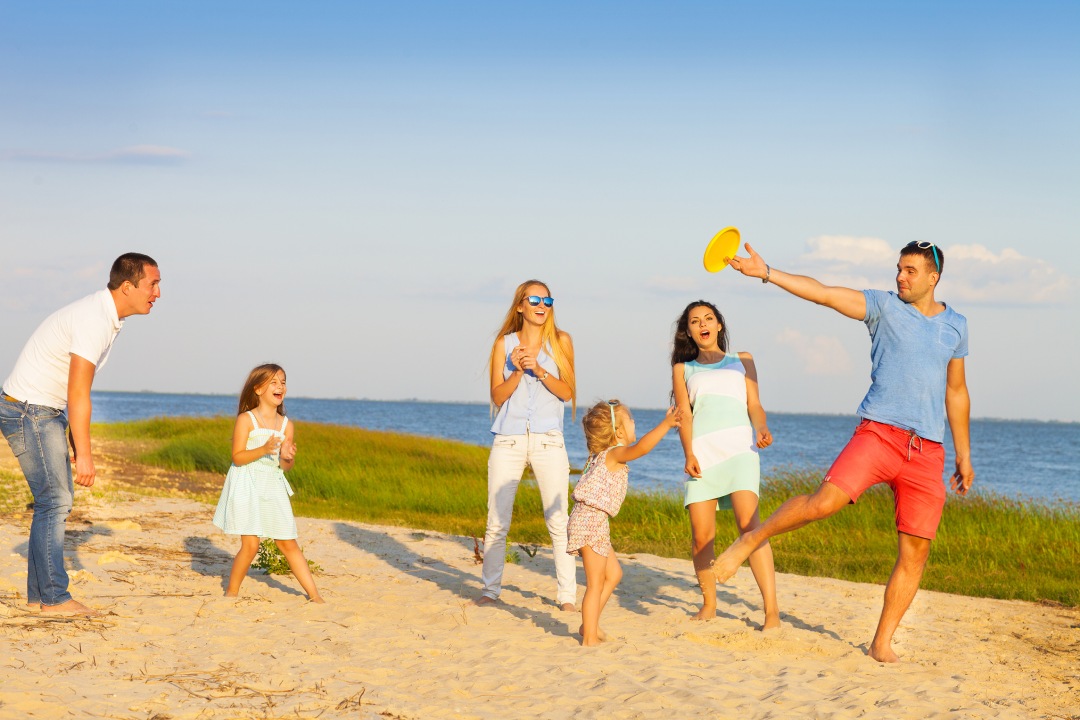 Friends with children playing with frisbee on the beach. Summer holiday and family concept