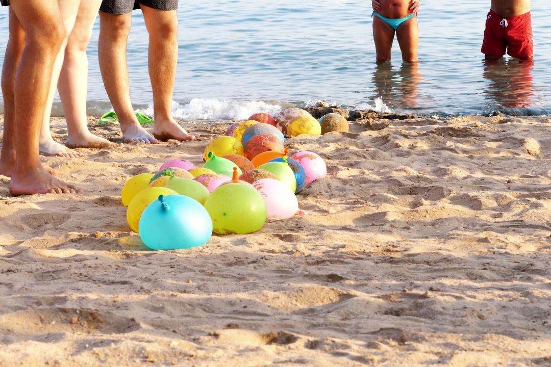 on the beach, on the sand are balloons filled with water instead of air. people having a rest playing fun games on the beach