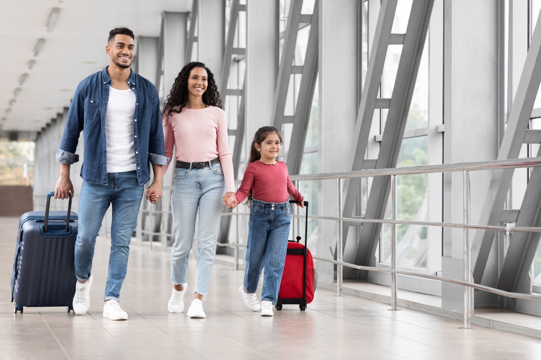 Travel Advertisement. Portrait Of Happy Arab Family Walking With Luggage At Airport, Beautiful Middle Eastern Mother, Father And Little Daughter Going To Boarding, Enjoying Traveling Together